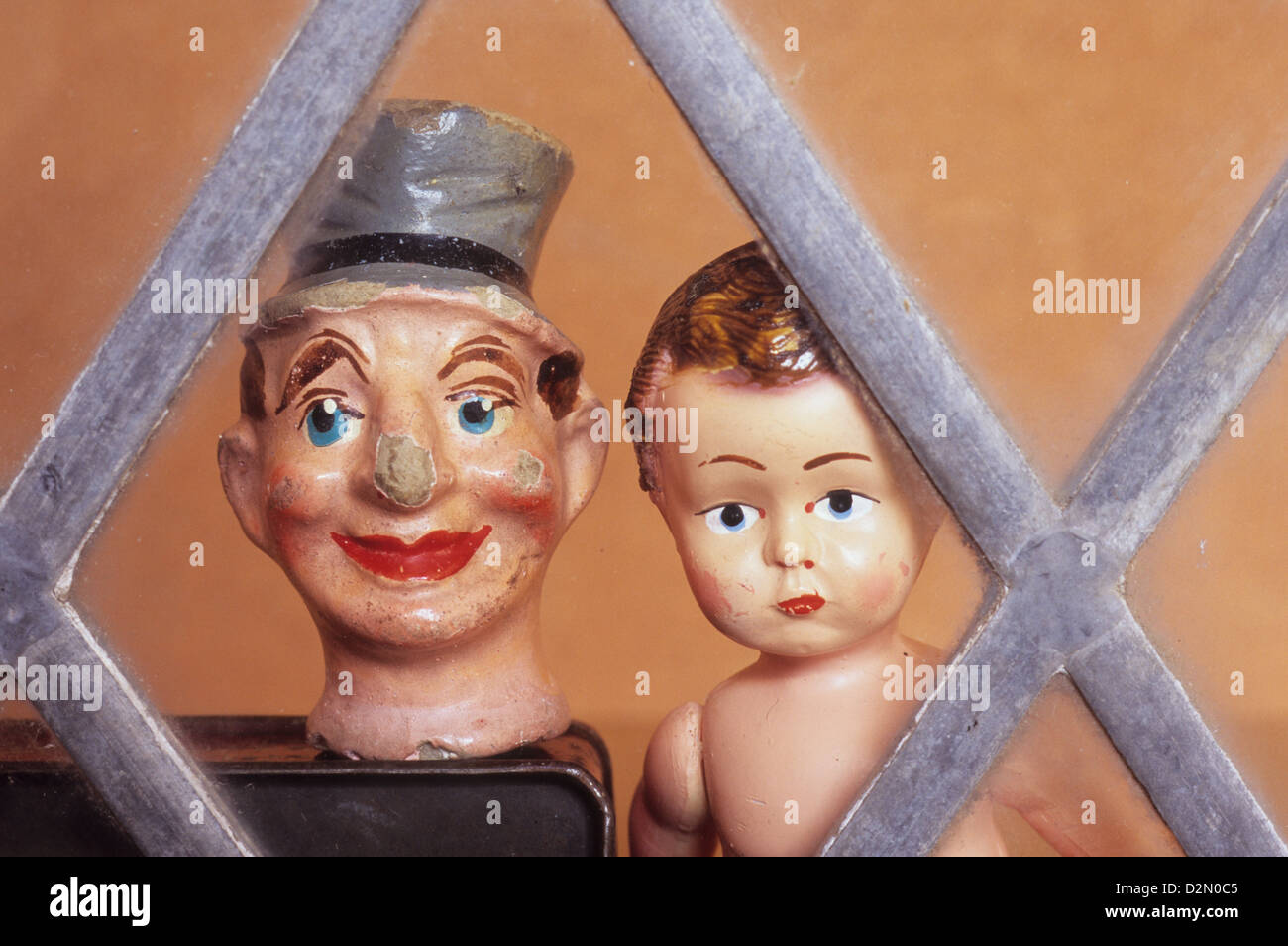 Battered and chipped papier mache male puppet head with top hat next to boy doll with sullen face looking through window Stock Photo