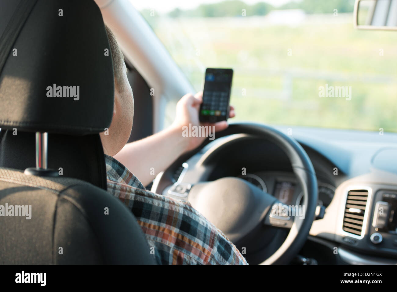 Texting and talking while driving, hands of young man on steering wheel Stock Photo