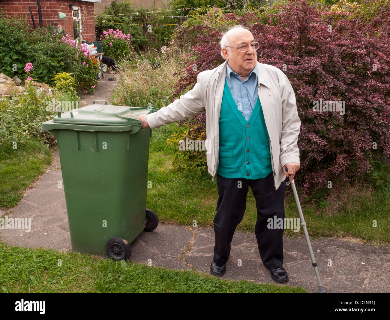 elderly man pulling green wheelie bin along garden path Stock Photo - Alamy