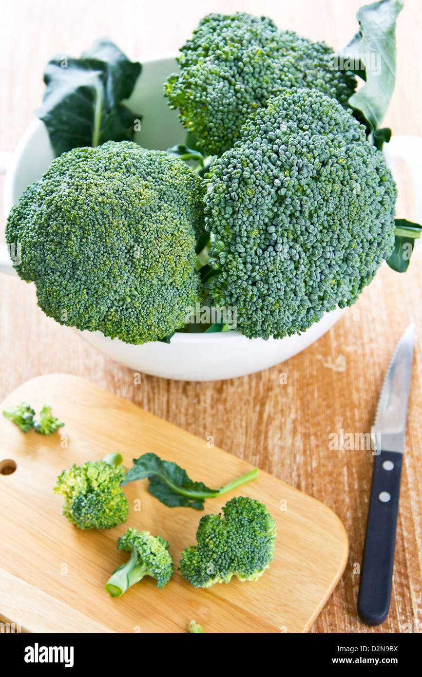Fresh uncooked broccoli in colander and chopping board Stock Photo