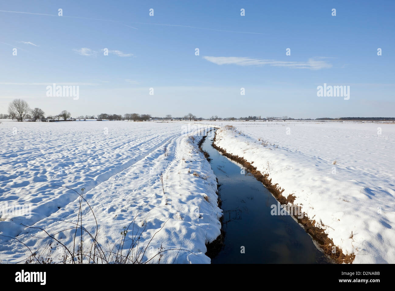 A freezing ditch set  in winter farmland with trees and hedgerows under a blue sky Stock Photo