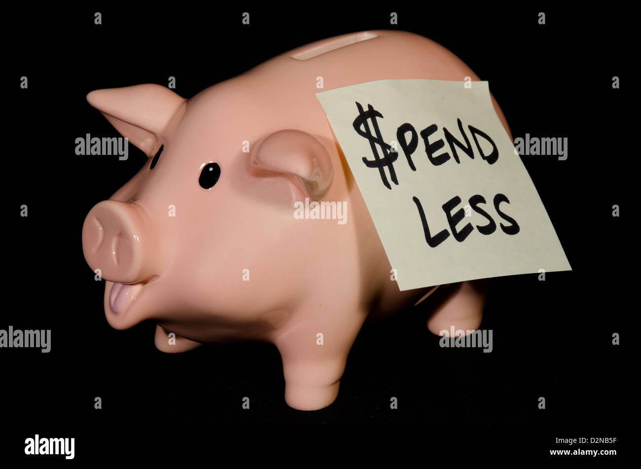This empty little piggy bank has a note on his side to remind him to spend less money and try to save it. Stock Photo