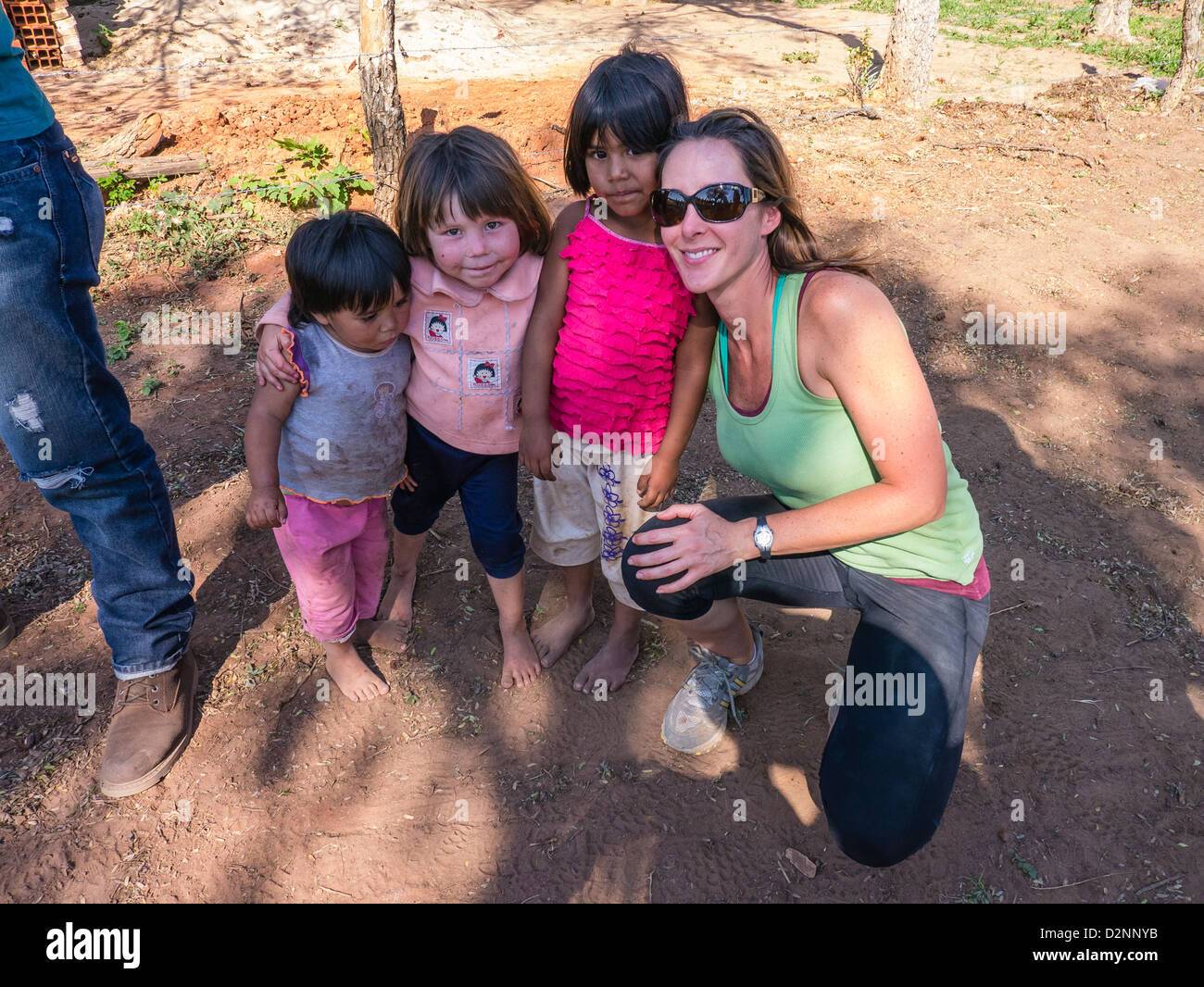 A female American volunteer for a Habitat for Humanity build in Paraguay poses with local children at the construction site. Stock Photo