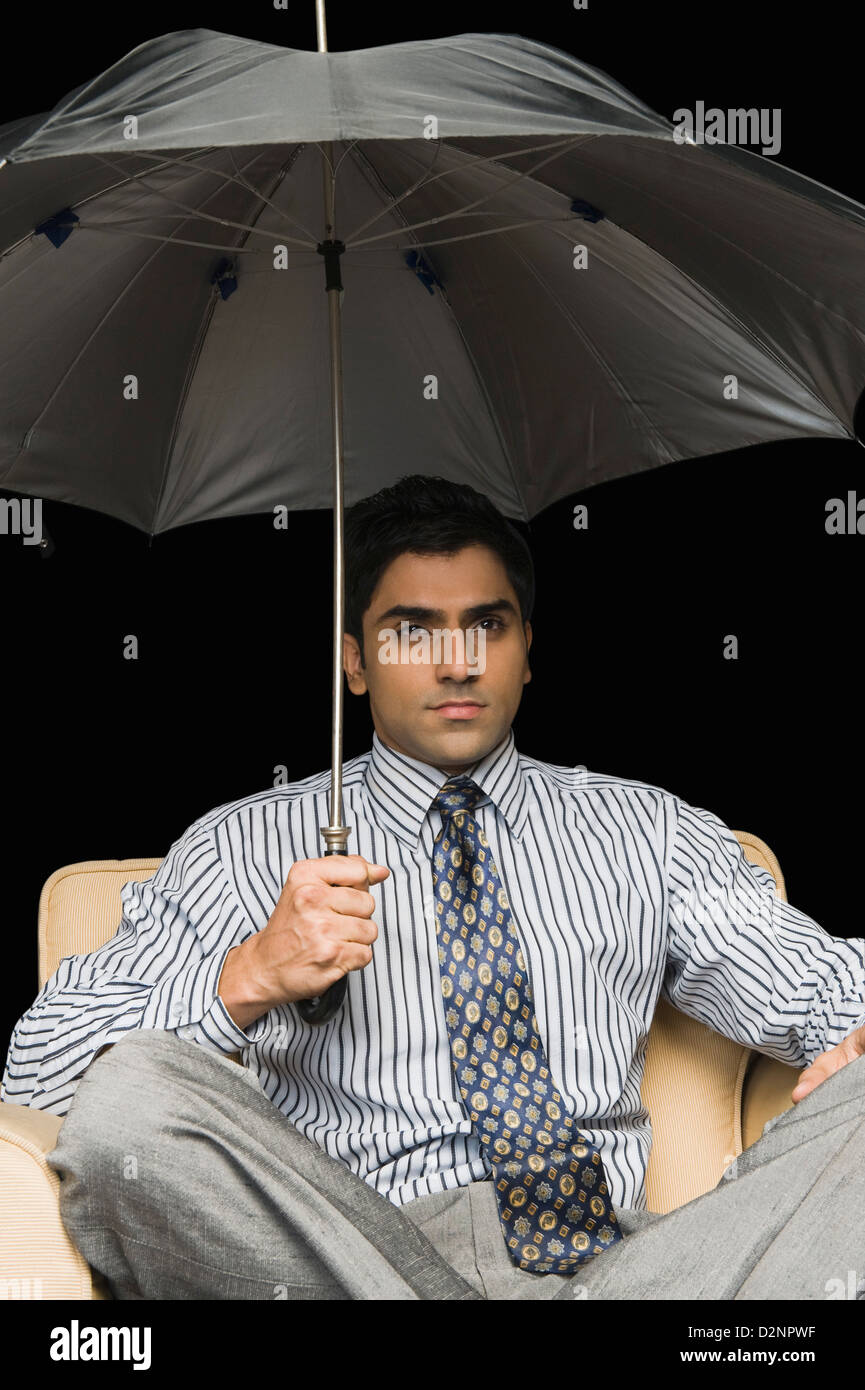 Businessman sitting in an armchair under open umbrella Stock Photo Alamy