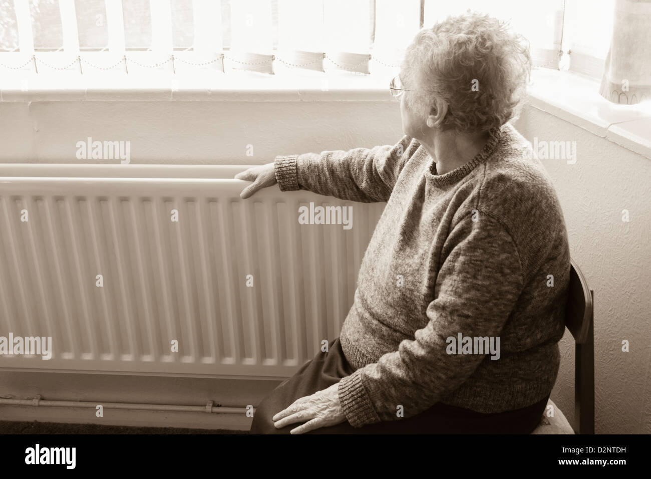 Ninety year old woman with hand on radiator looking out of window, UK. Coronavirus, self isolation, social distancing, quarantine... concept Stock Photo