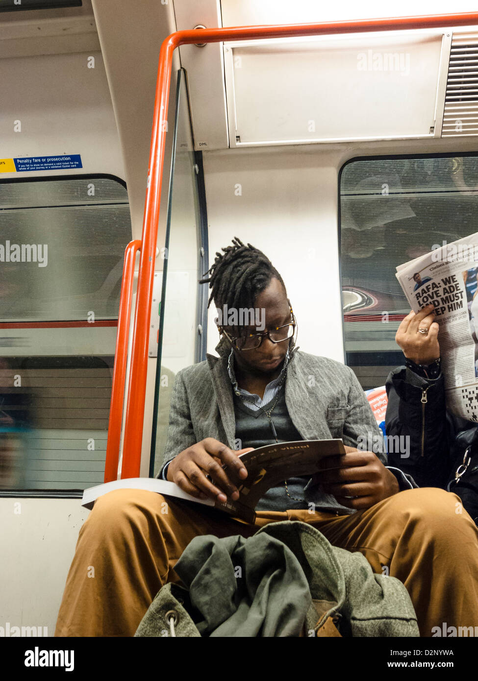 a man with dreads and hglasses is reading from a textbook in London underground Stock Photo