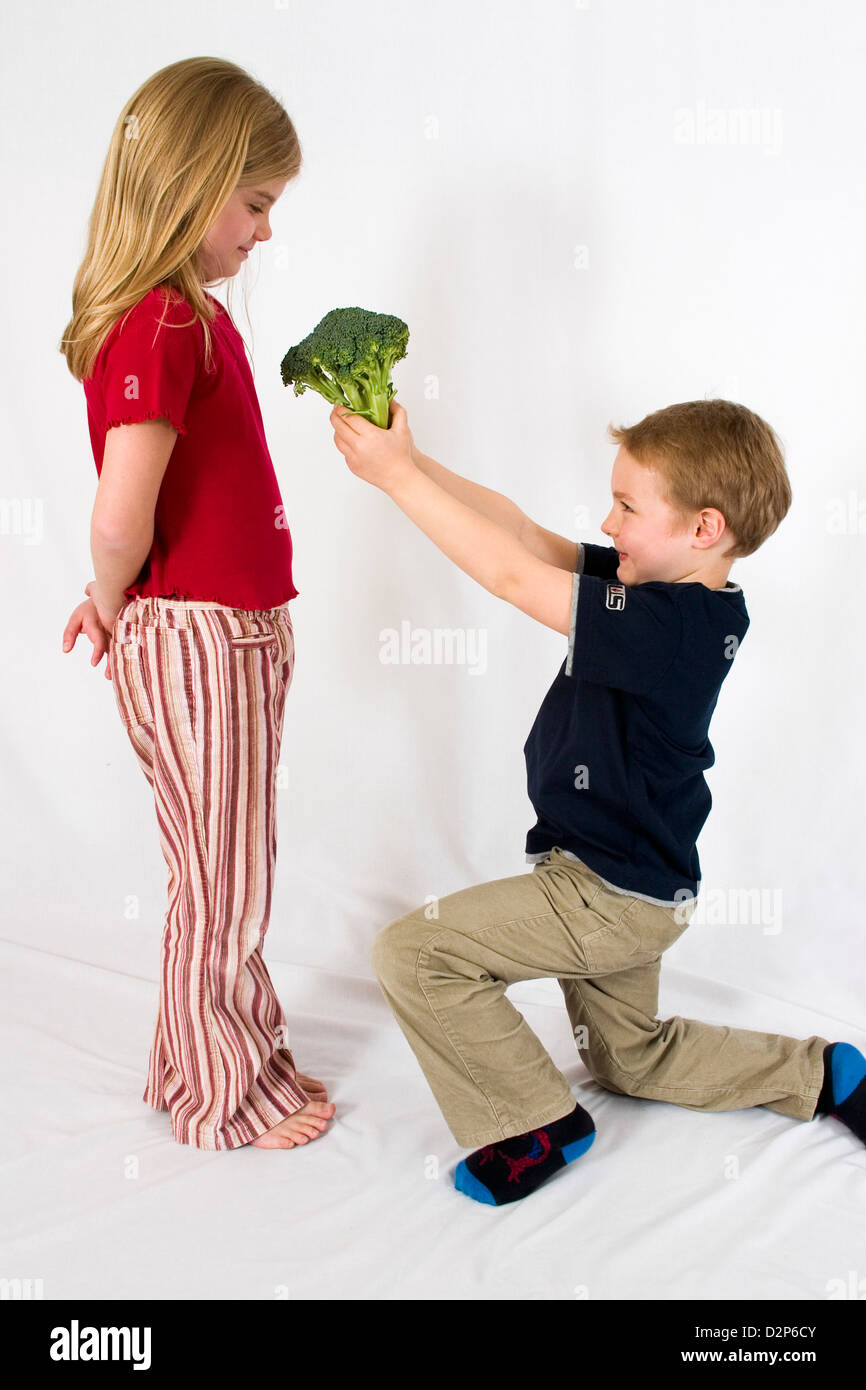 Young healthy children playing with a head of green broccoli. Boy gives the broccoli to the girl