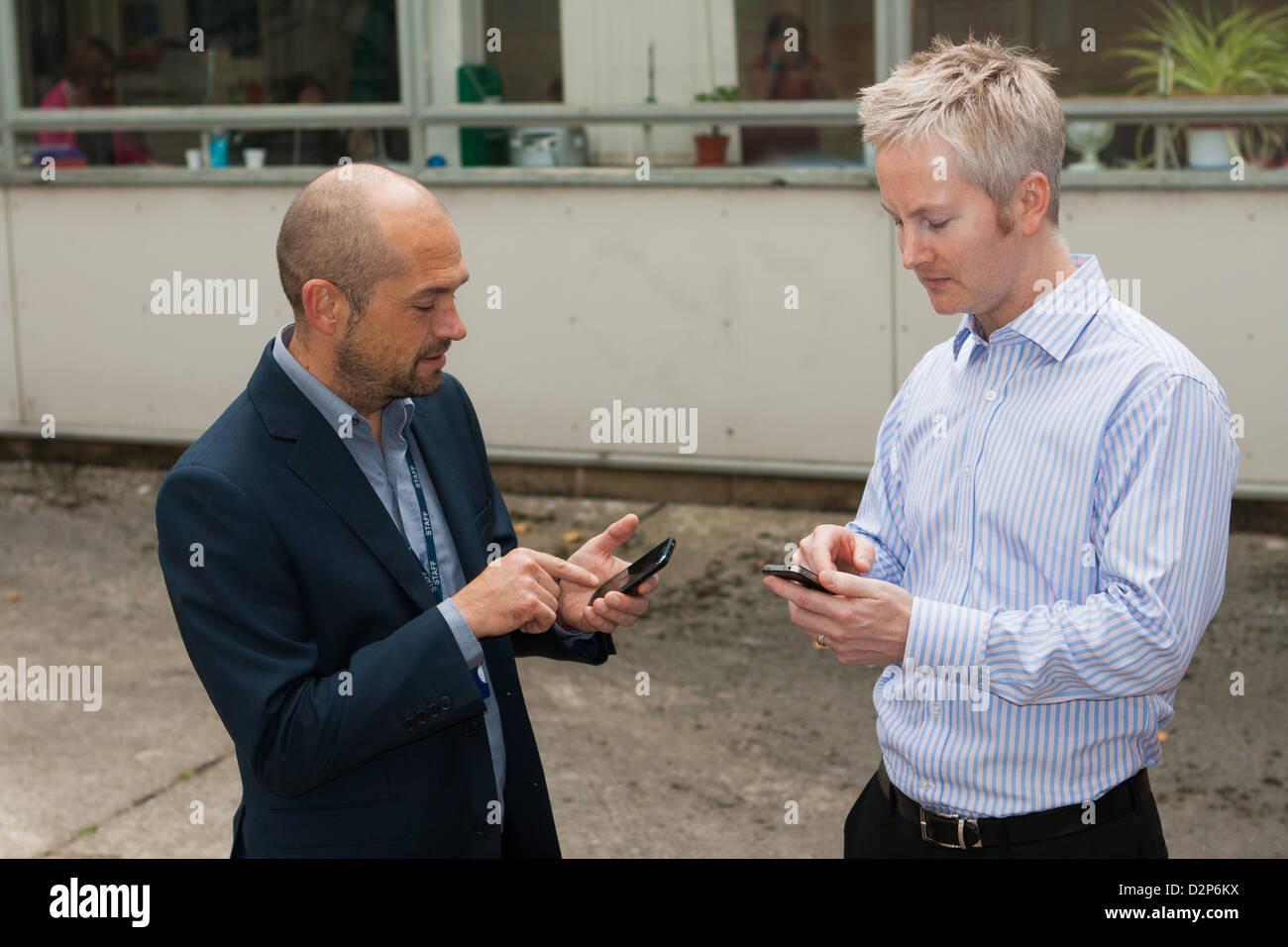 Two men texting on their mobile phones. Stock Photo