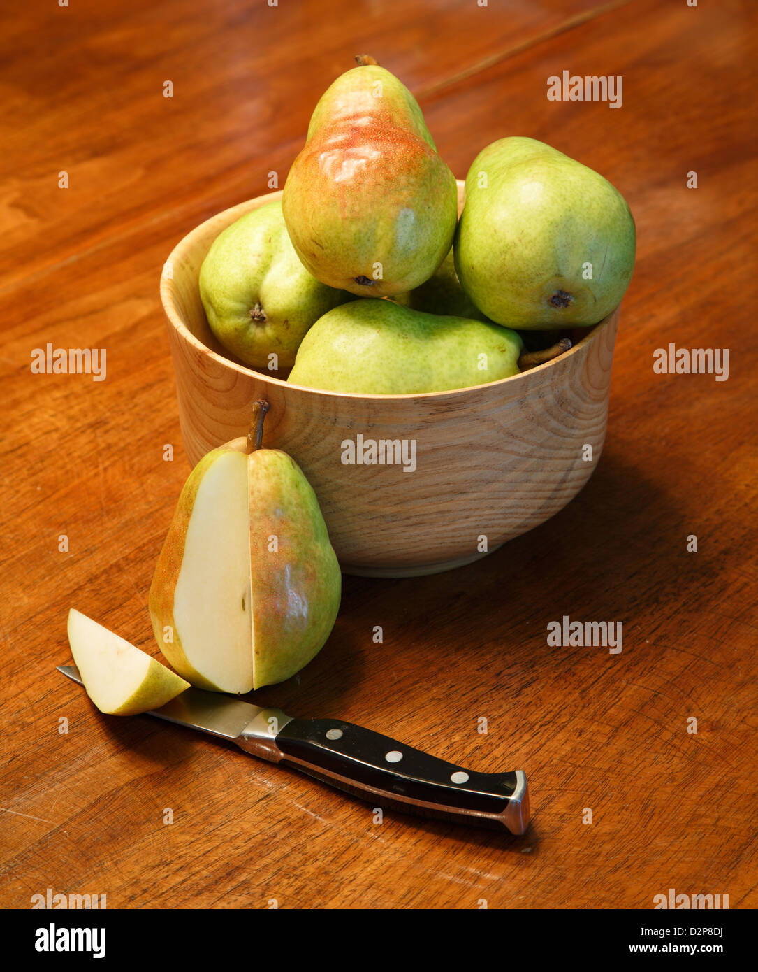 Fresh bartlett pears in a wood bowl on a table with one cut by paring knife Stock Photo