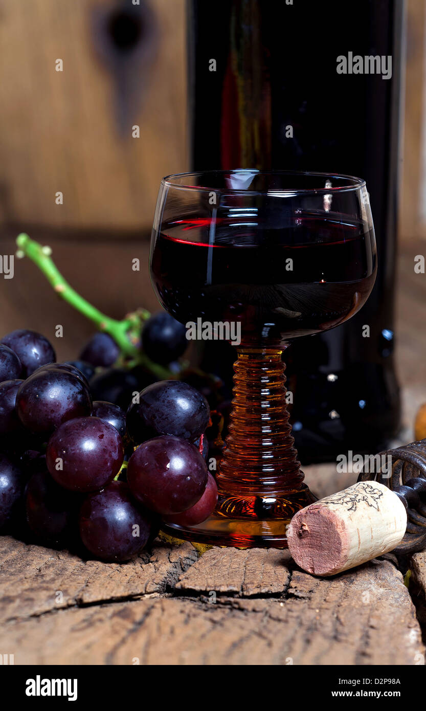 A glass of red wine with bottle and grapes are on a rustic old wooden ...