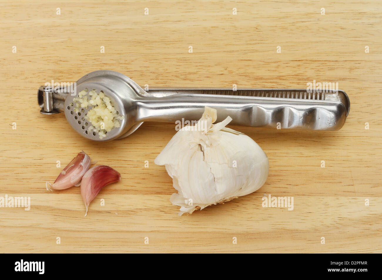 Garlic press with a garlic bulb and cloves on a wooden board Stock Photo