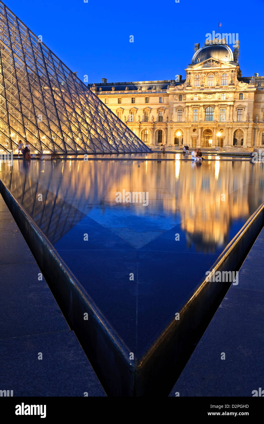Paris, Louvre Museum, illuminated glass pyramid, nighttime, with reflections in the foreground pool.