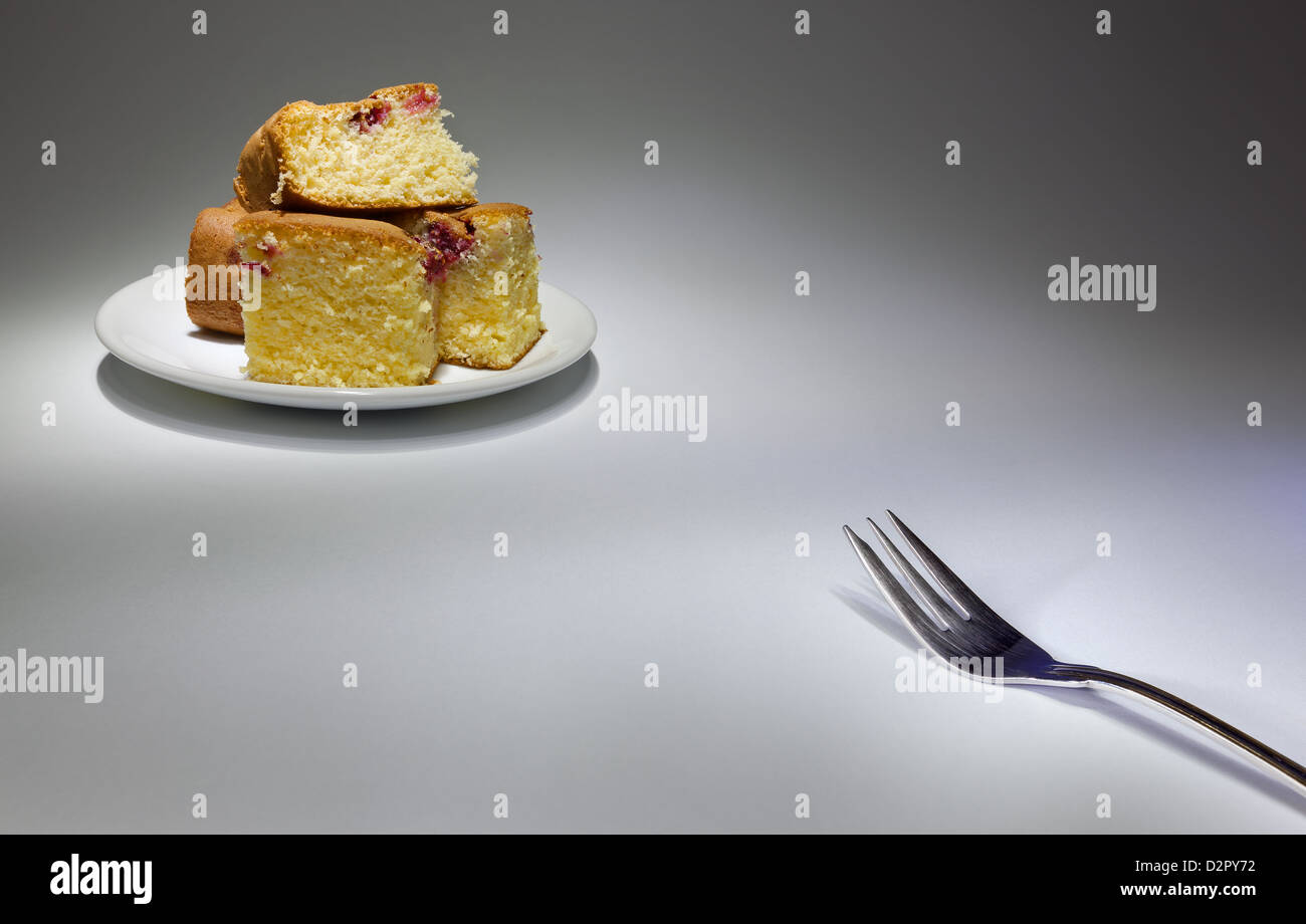 Metal fork in one corner and some cakes on white plate in other corner. Stock Photo