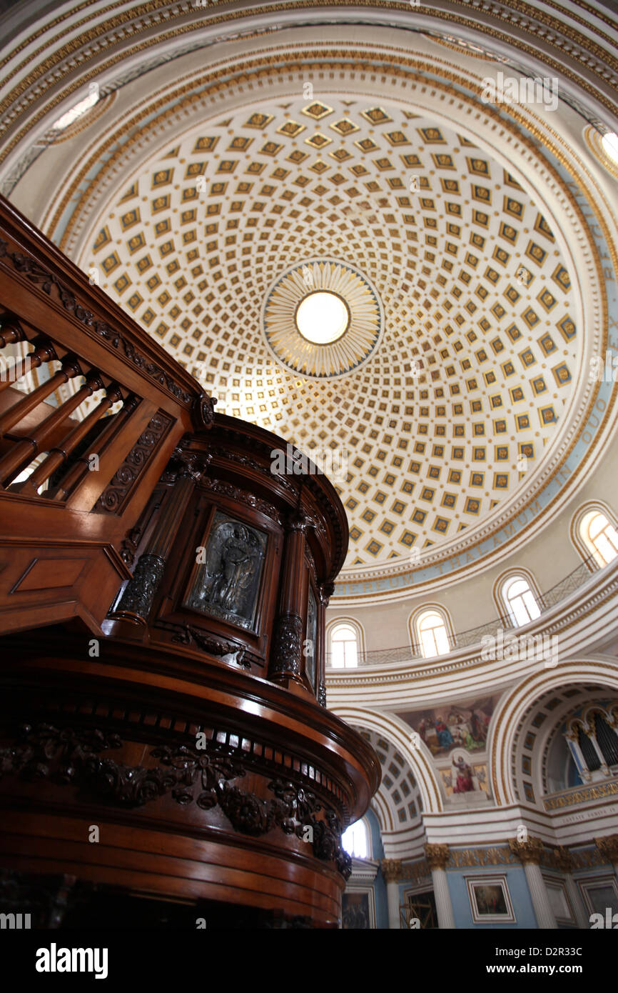 A ornately carved wooden pulpit and the Mosta Dome ceiling interior in the background Stock Photo