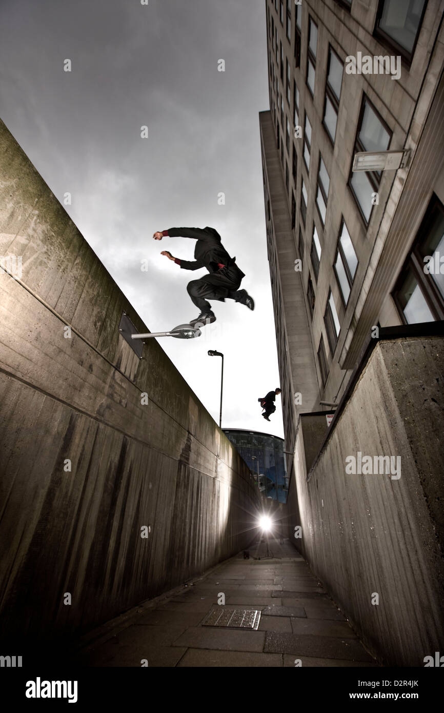 Parkour runners in suits jumping urban alleyway Stock Photo