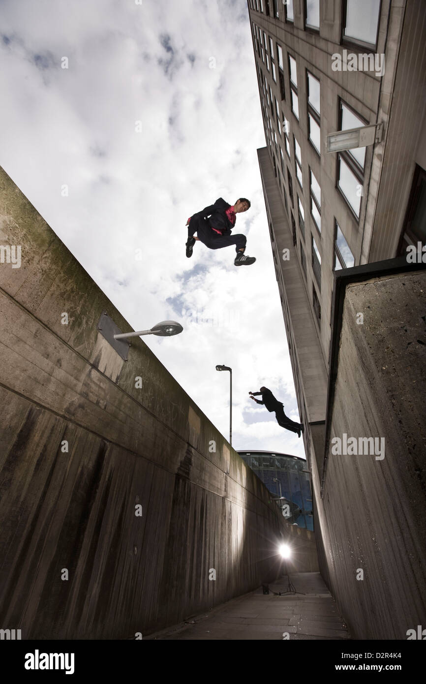 Parkour runners in suits jumping urban alleyway Stock Photo
