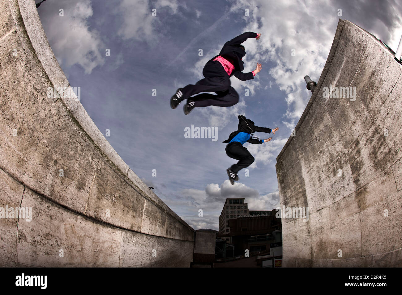 Parkour runners in full suit jumping between concrete roofs Stock Photo