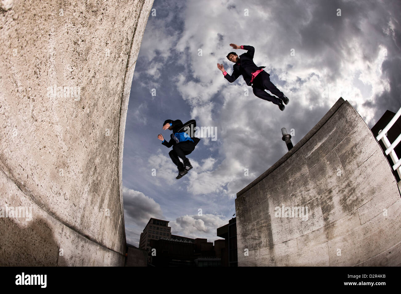 Parkour runners in full suit jumping between concrete roofs Stock Photo