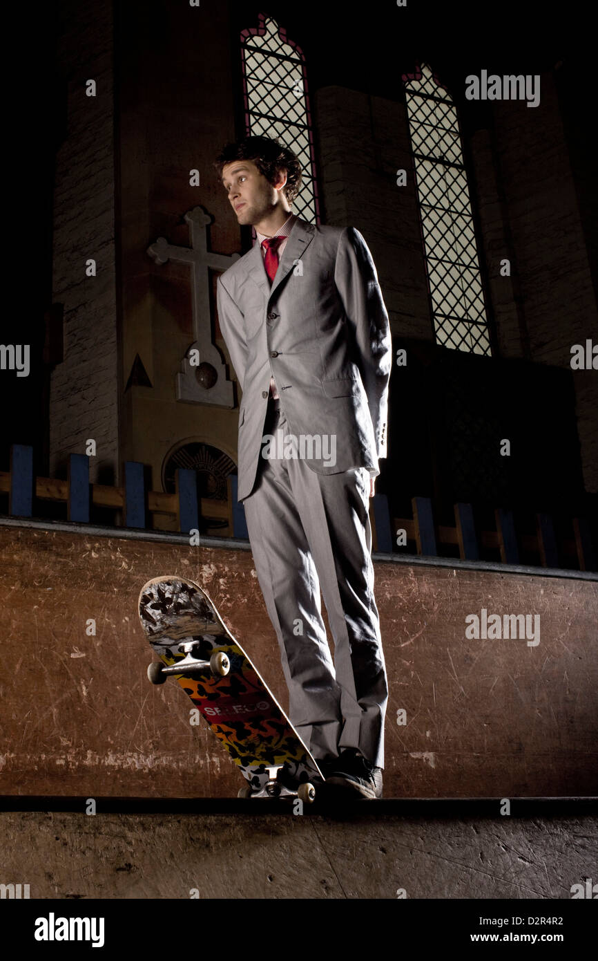 Skateboarder in full suit stands with skateboard at night inside church Stock Photo