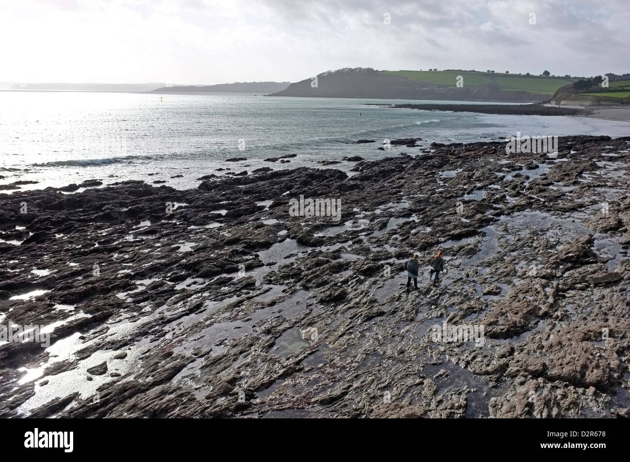 Two young women walk along the rocks on Gyllingvase beach in Falmouth, Cornwall Stock Photo