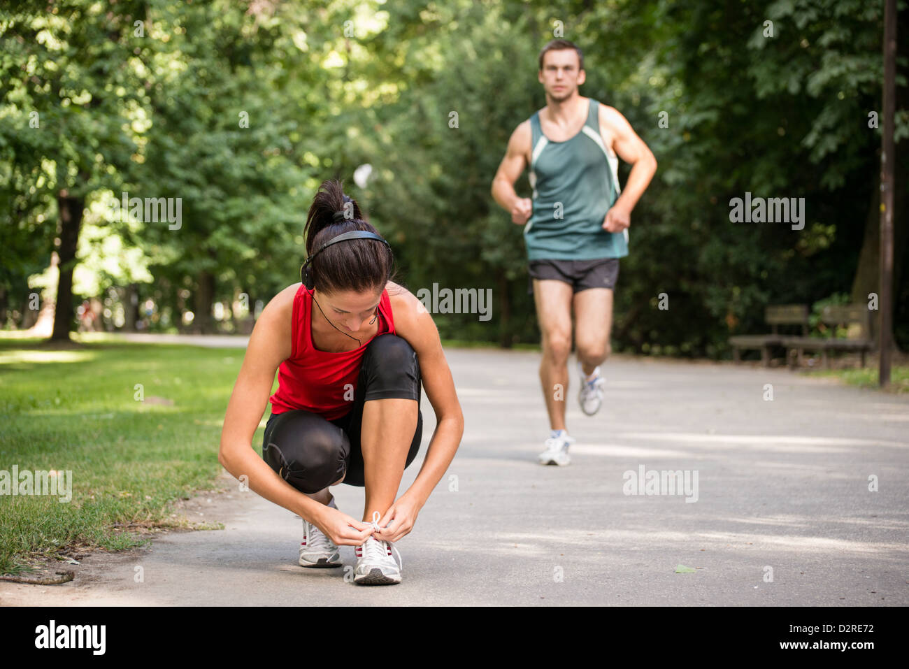 Young sport woman tying shoelace, man in behind is jogging Stock Photo