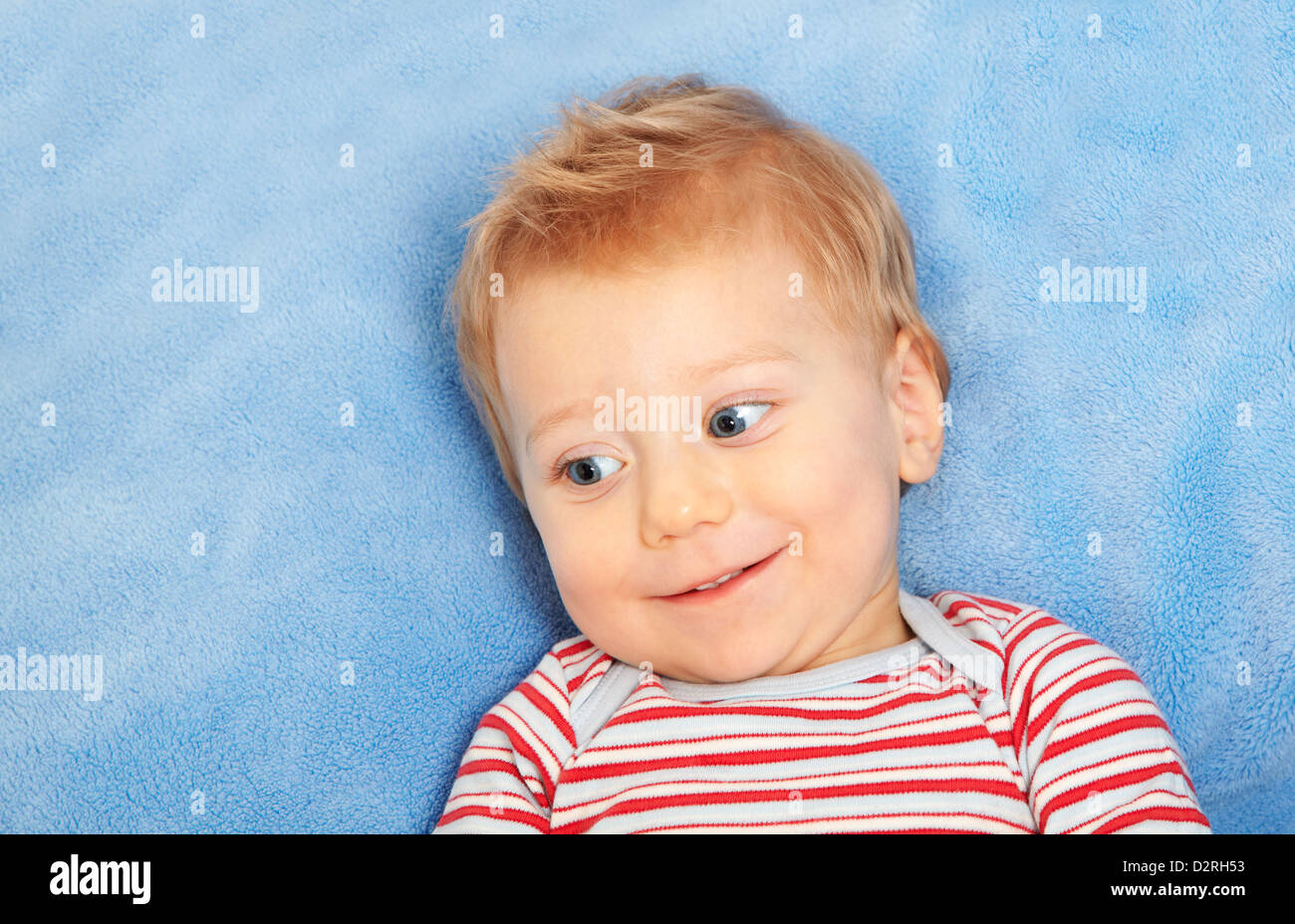 Studio portrait of a happy one year old baby boy smiling and laying down on blue blanket Stock
