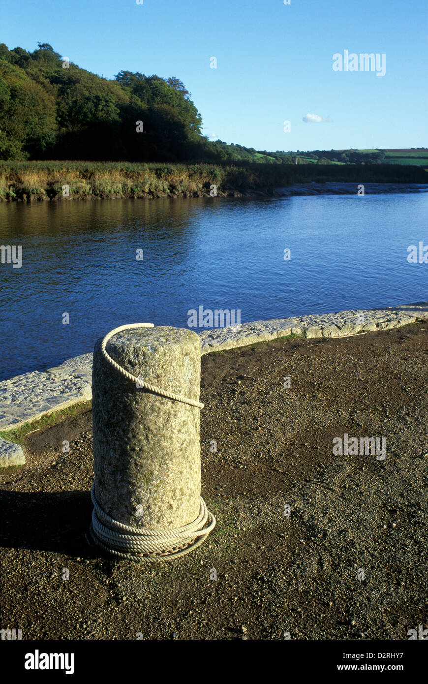 Quayside granite bollard with the River Tamar, Cothele Quay, St Dominick, Cornwall, England, UK Stock Photo