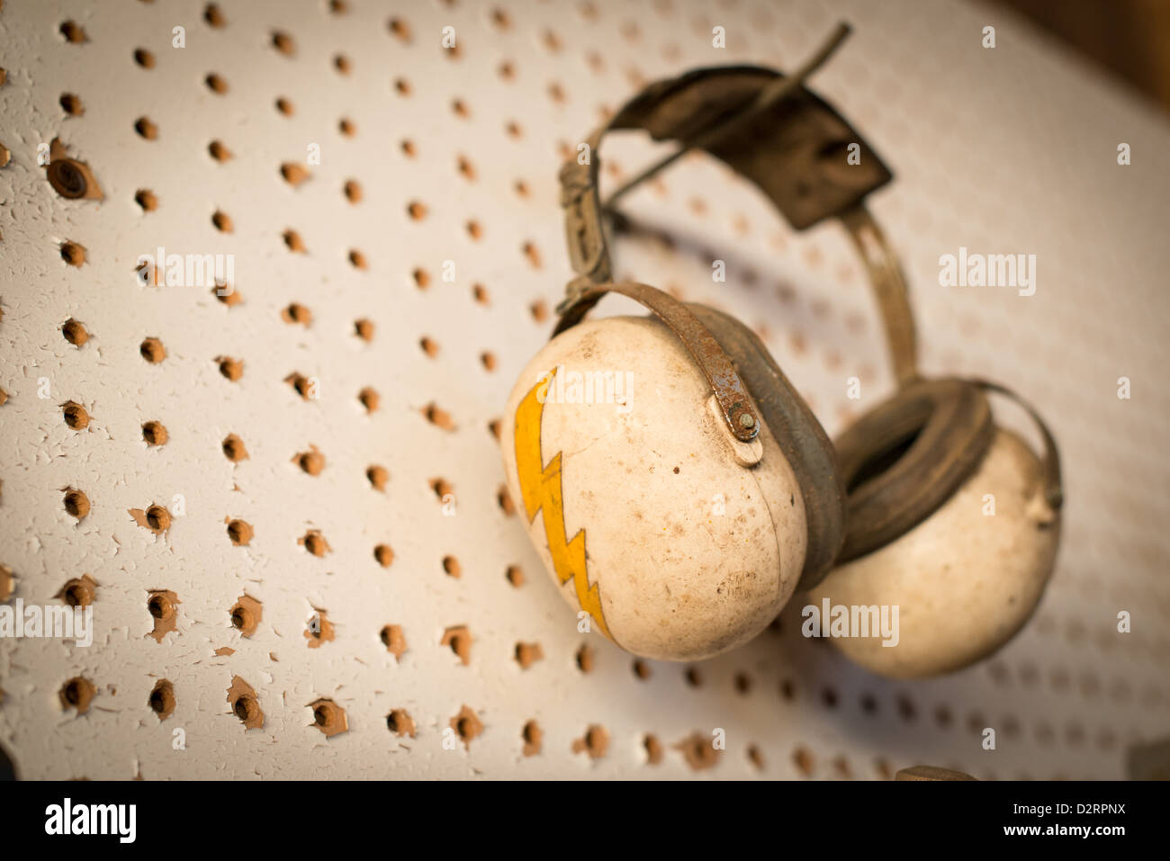 A pair of old earmuffs for hearing protection hangs on a wall. A bolt