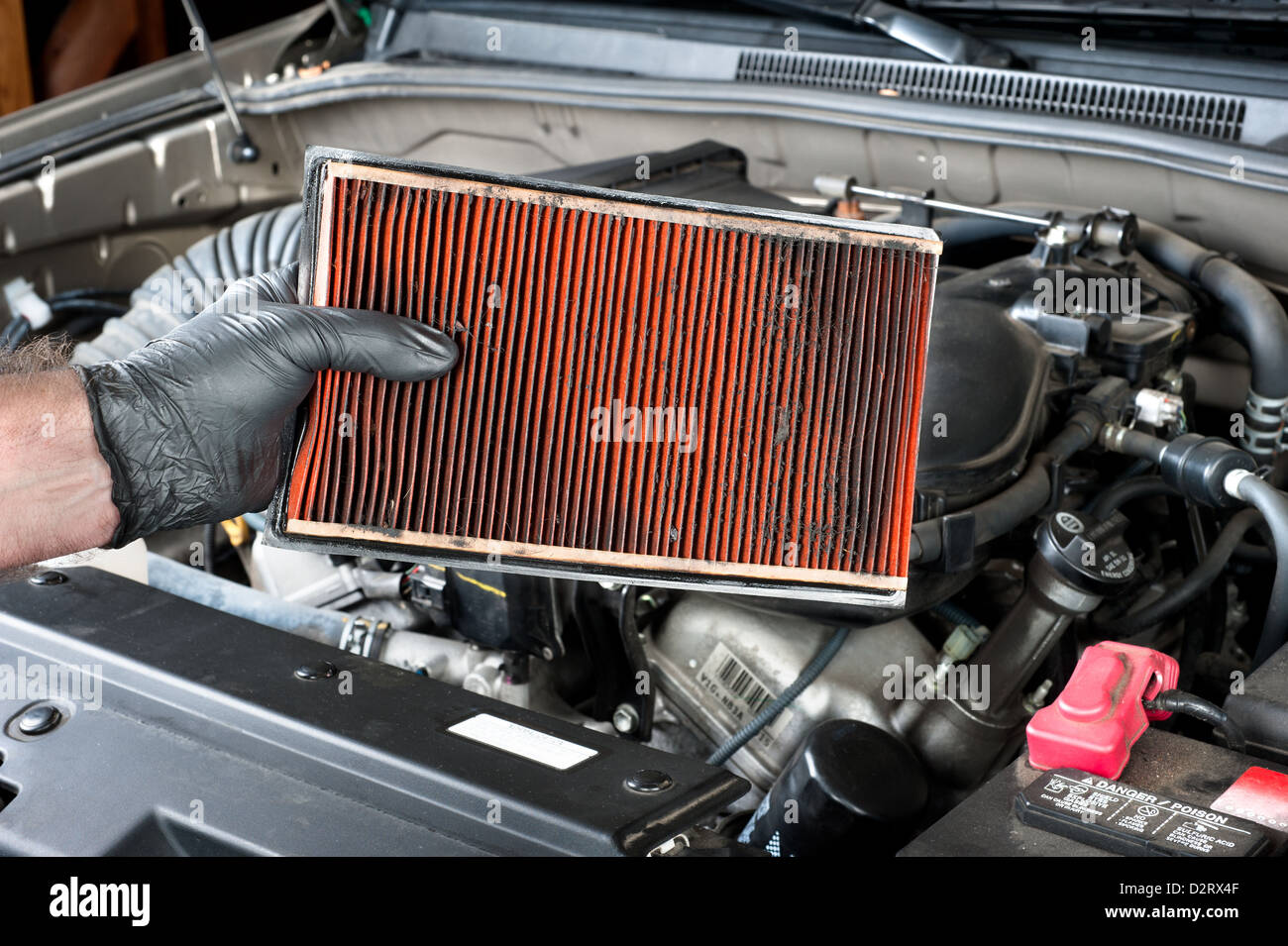 An auto mechanic wearing protective work gloves holds a dirty, clogged air filter Stock Photo