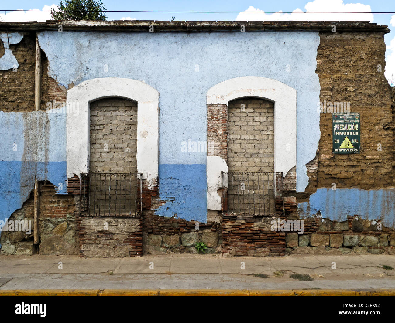 street facade abandoned adobe house with crumbling blue plaster & posted sign warning of building in bad condition Oaxaca Mexico Stock Photo