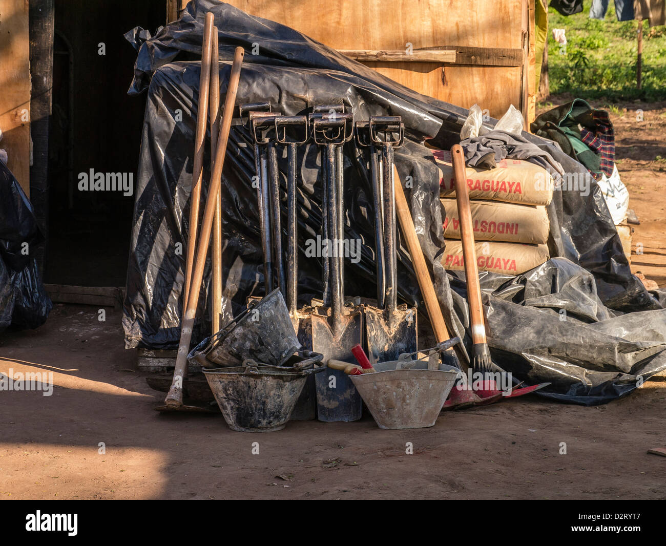 Shovels, picks, hoes, buckets and cement are stored outside of a shack ready for use by Habitat