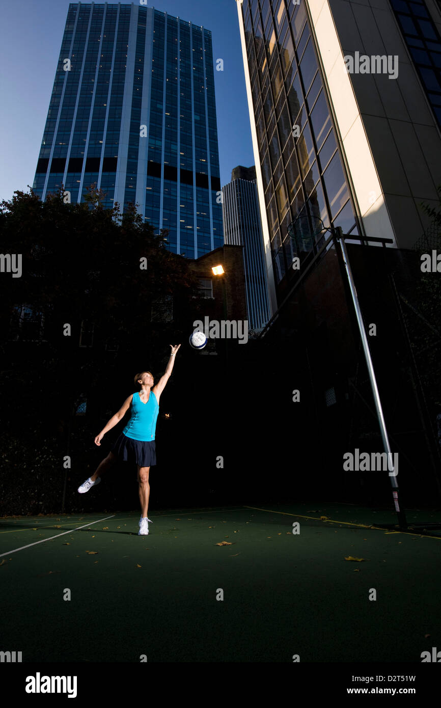 Netball player aiming at net on urban pitch Stock Photo