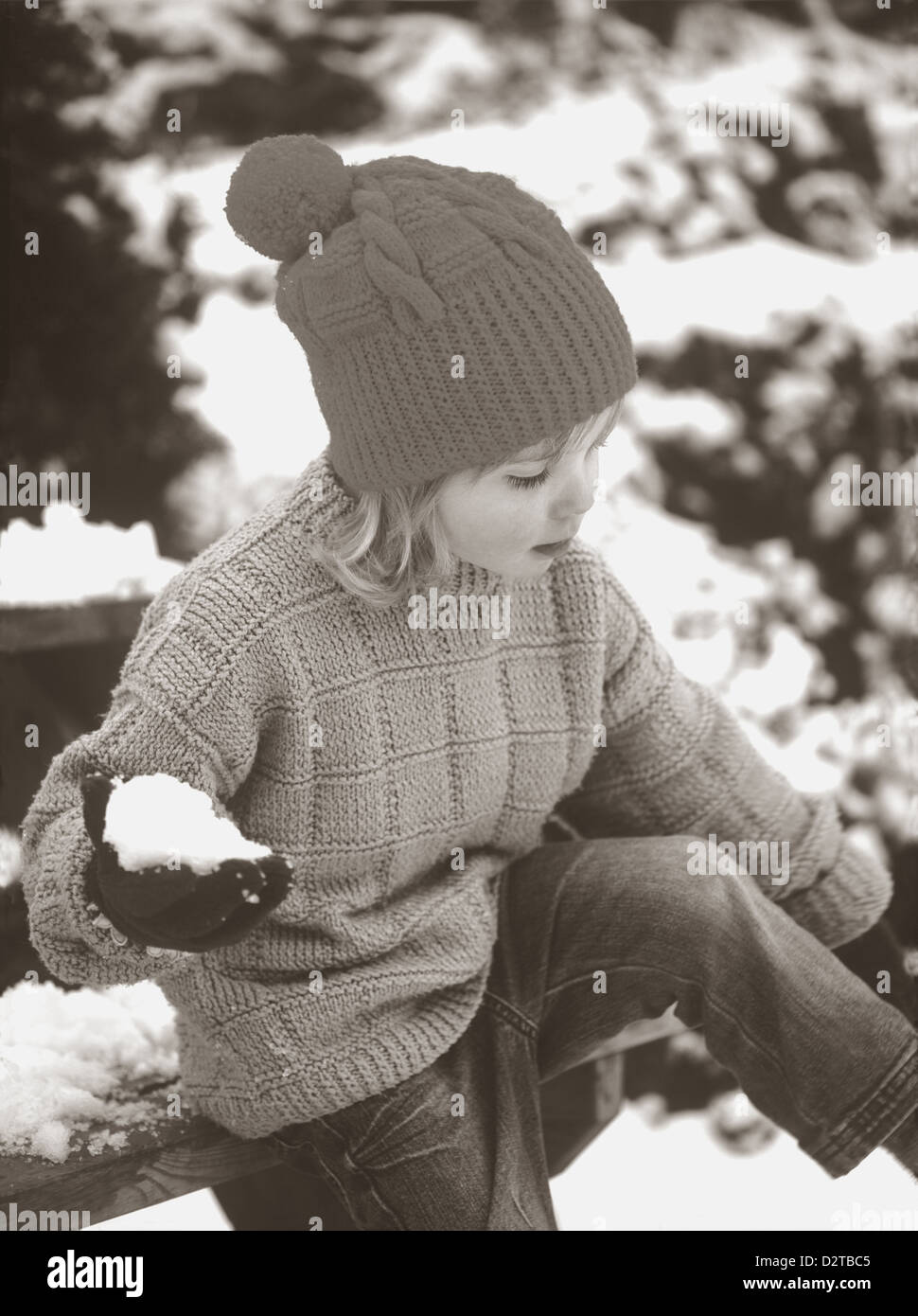 Vintage style photo of Young girl wearing vintage-style jumper and hat, holding a snowball in wintertime in Cornwall, England, U.K. Stock Photo