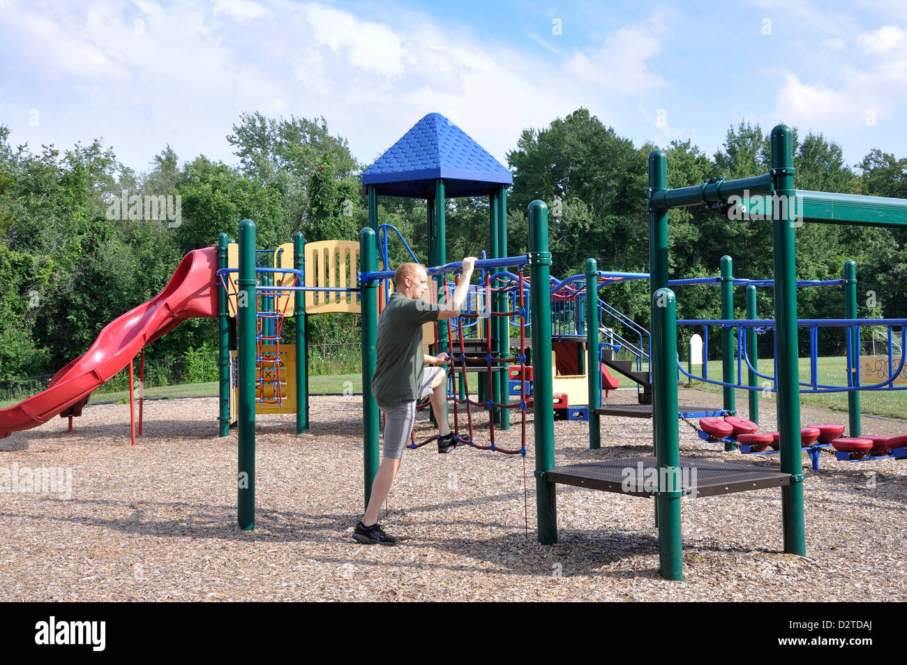 Adult man climbing in a children's playground as if he recalls his childhood Stock Photo