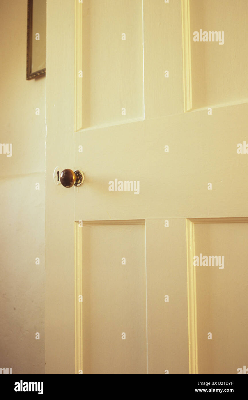 Detail of old internal wooden panelled door painted white with brass knob standing open to reveal wall with mirror Stock Photo