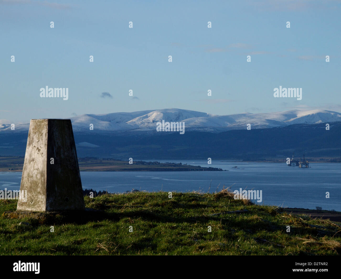 Looking past a Trig point over the Cromarty Firth to Ben Wyvis in the Scottish Highlands, with Oil Rigs moored near Invergordon. Stock Photo