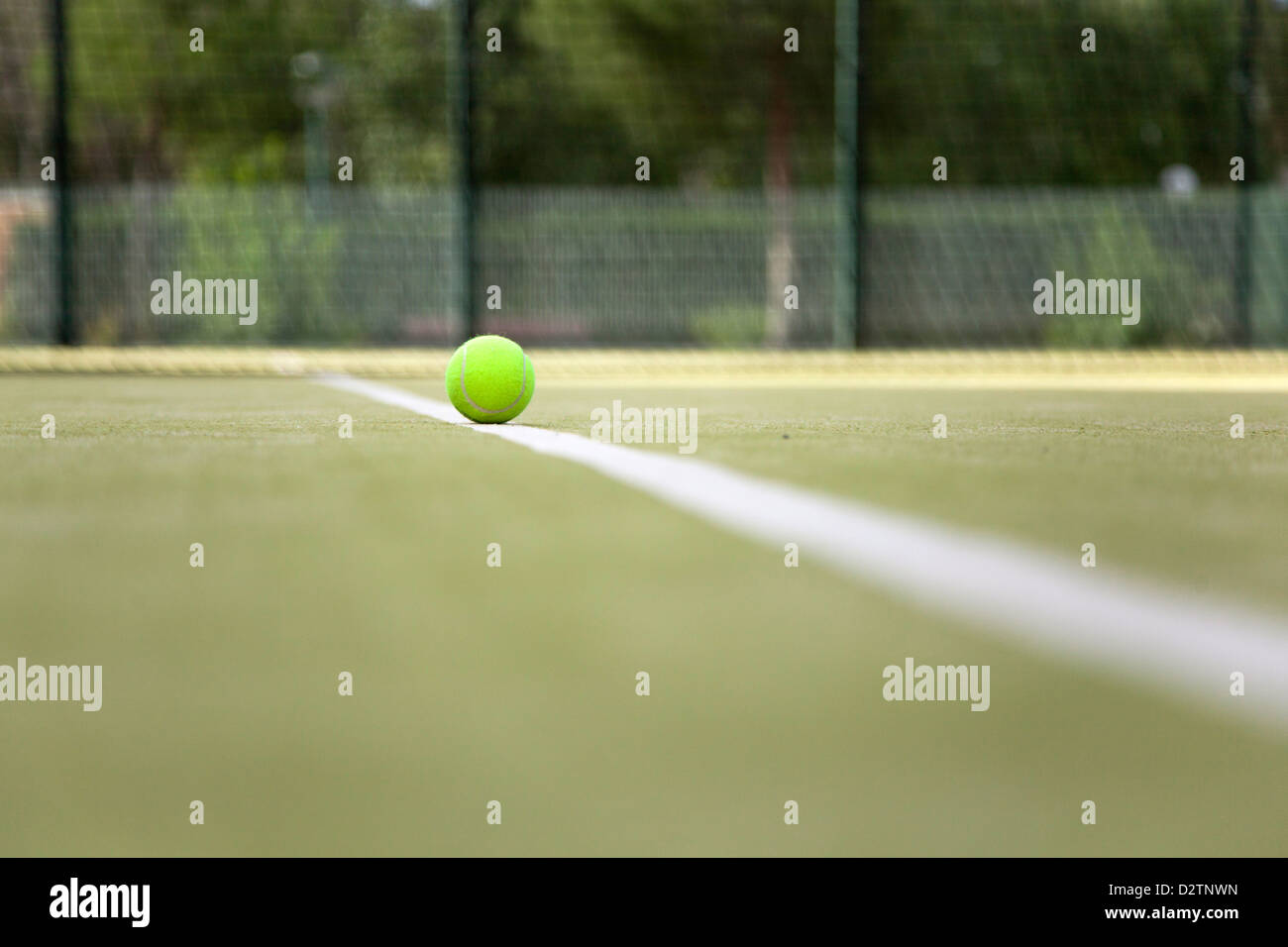 Close-up of a fluffy yellow tennis ball on the white line of a paddle court. Stock Photo