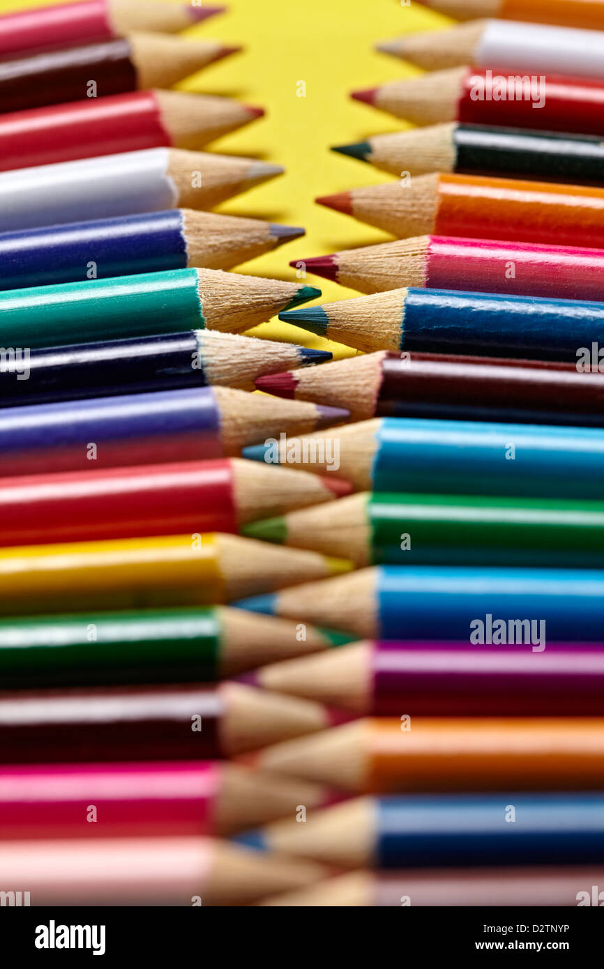 Coloured pencils aligned like a zip interlaced together on a yellow background Stock Photo