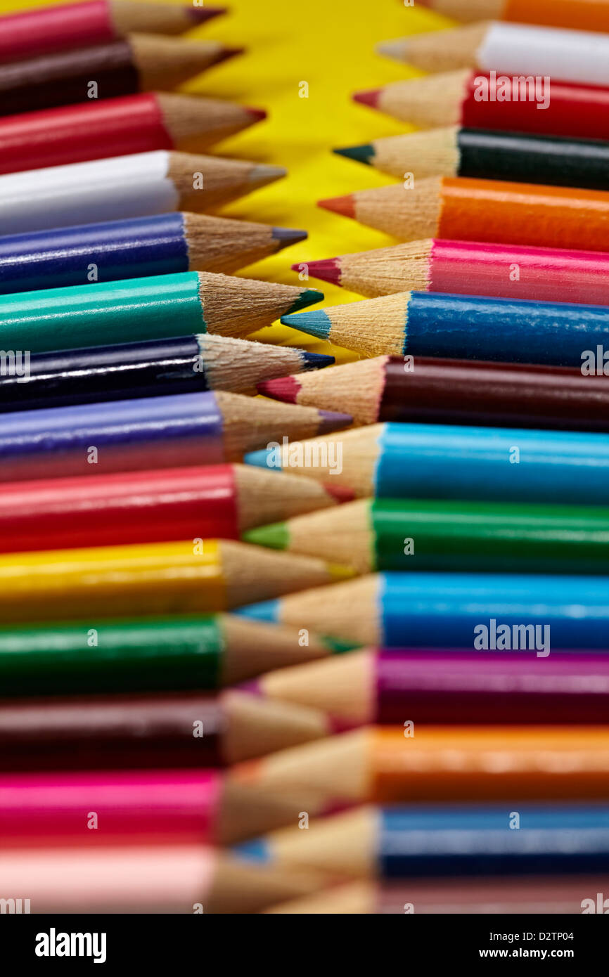 Coloured pencils aligned like a zip interlaced together on a yellow background Stock Photo