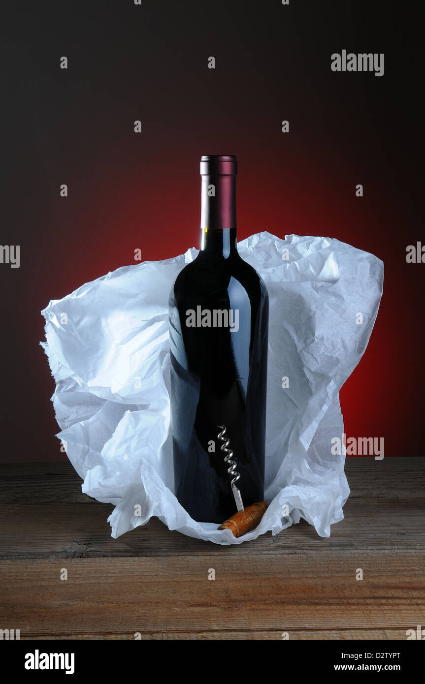 Red Wine Bottle and Cork Screw with tissue paper wrapping on wood surface and light to dark background. Stock Photo