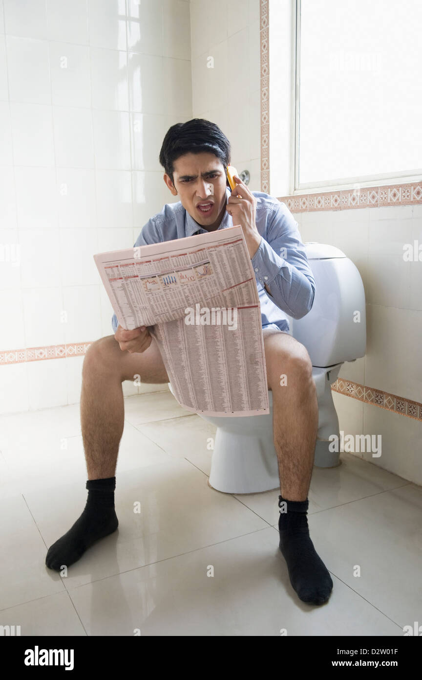 Businessman talking on a mobile phone and reading a newspaper on a ...