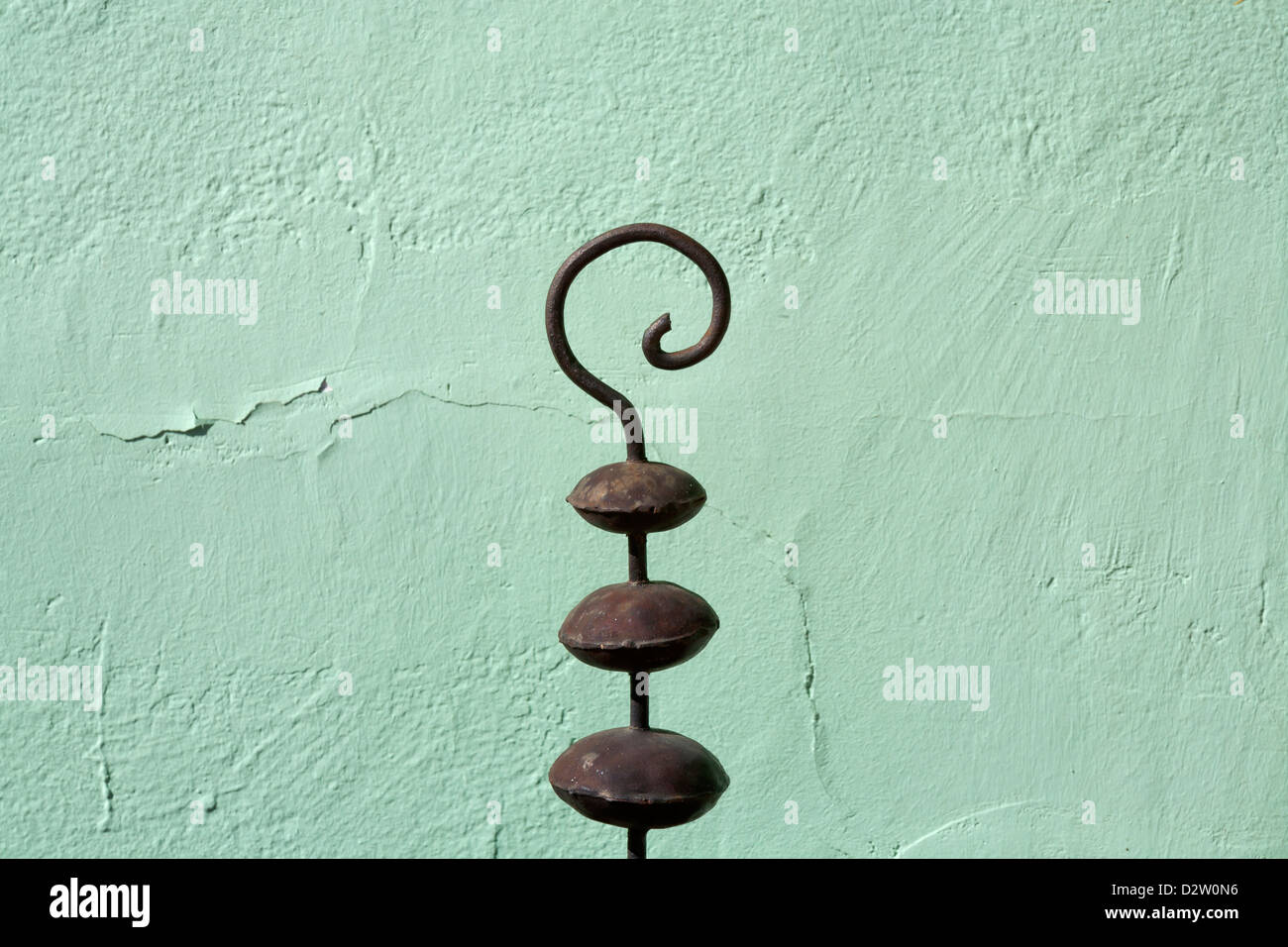 Decorative metal crook like object in front of a green/blue textured wall Stock Photo