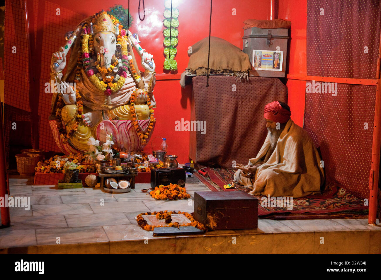 India, Rishikesh. Hindu Priest Sitting in a Shrine to Ganesh. Stock Photo
