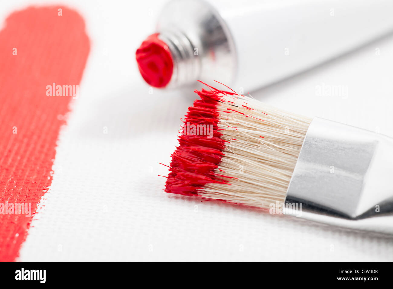 Red paint on paint brush with tube of acrylic paint and paint stroke on canvas Stock Photo