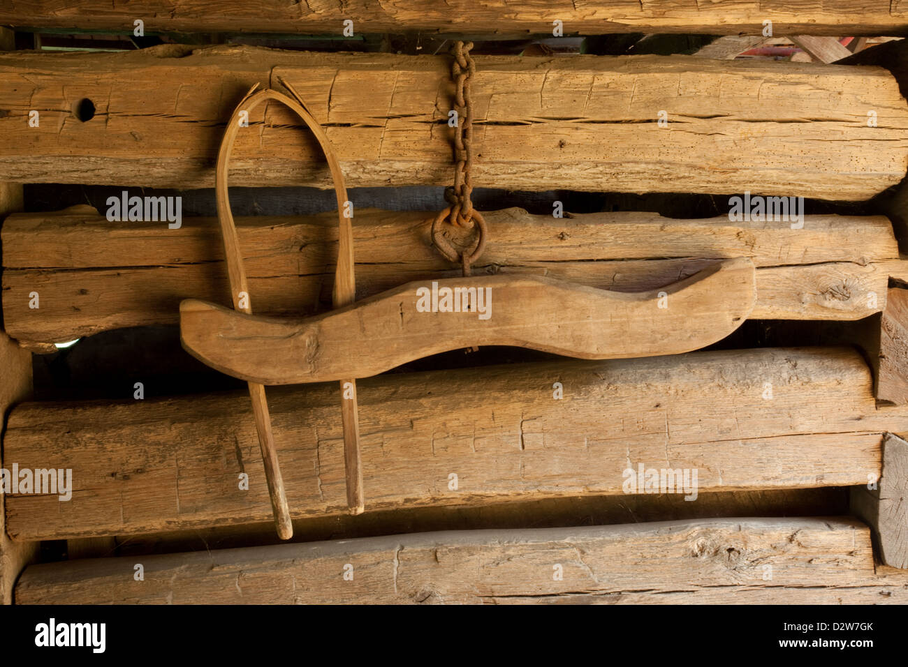 Half of an ox yoke, hanging on some rough walls, suspended by a rusty chain Stock Photo