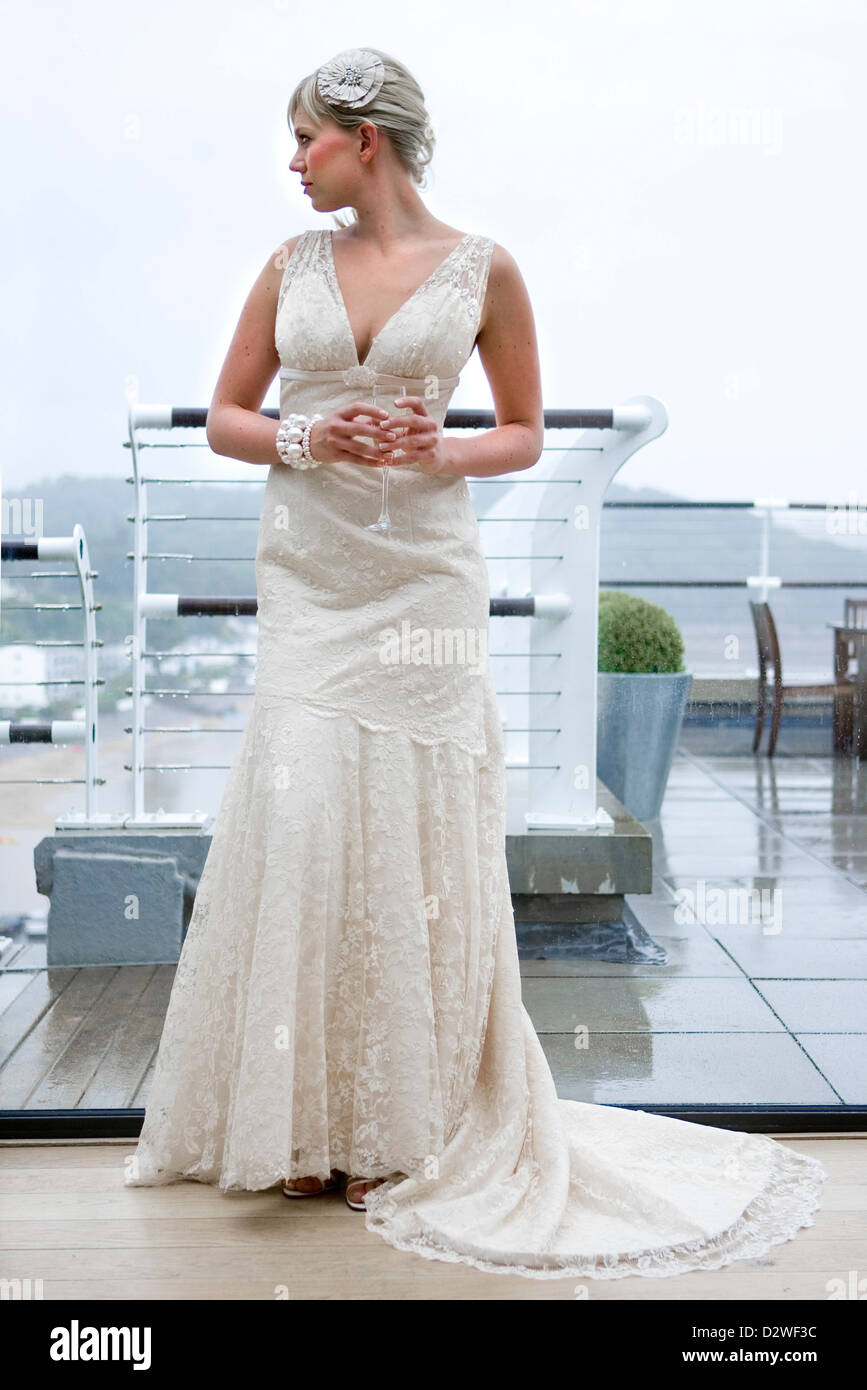 A pretty young blond bride looking out of a window as she waits for her wedding ceremony. Stock Photo