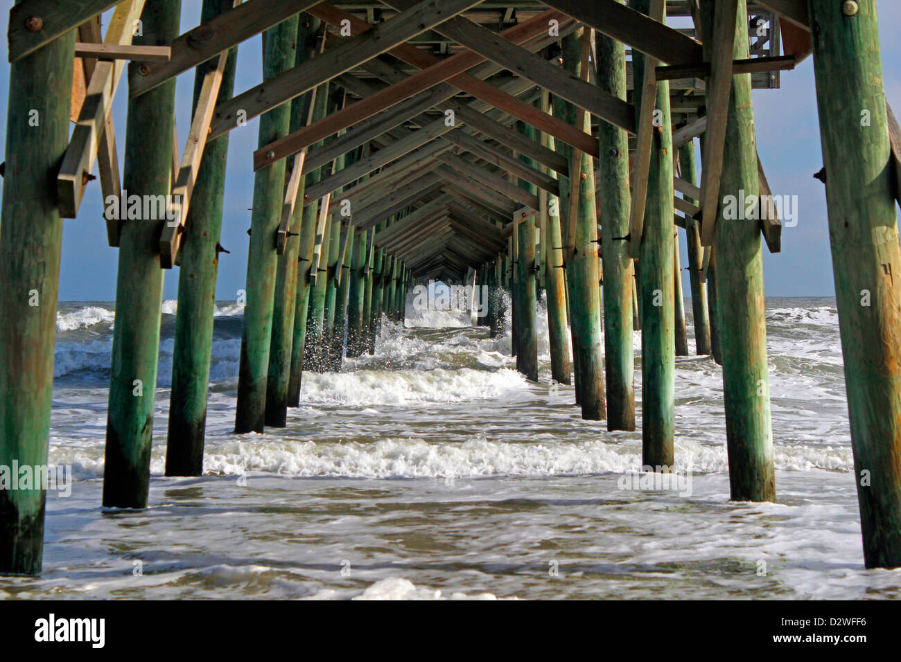 The underside of a fishing pier extending out through the surf. Stock Photo