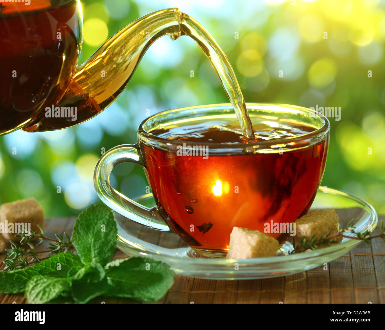 Pouring tea from a teapot into a cup on a blurred background of nature. Stock Photo