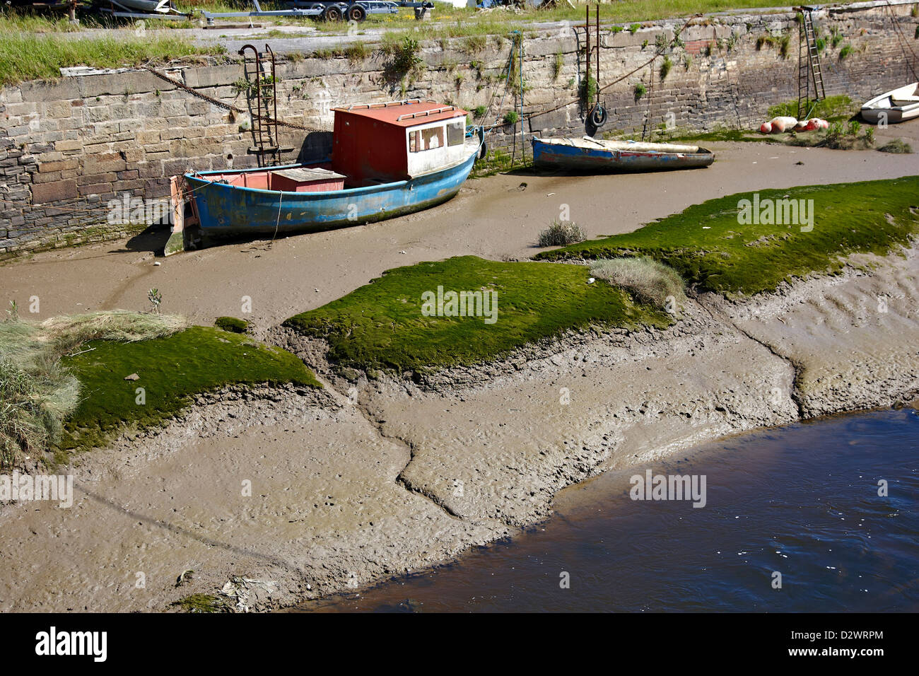 Boats resting on mud banks at low tide up against a retaining wall Stock Photo