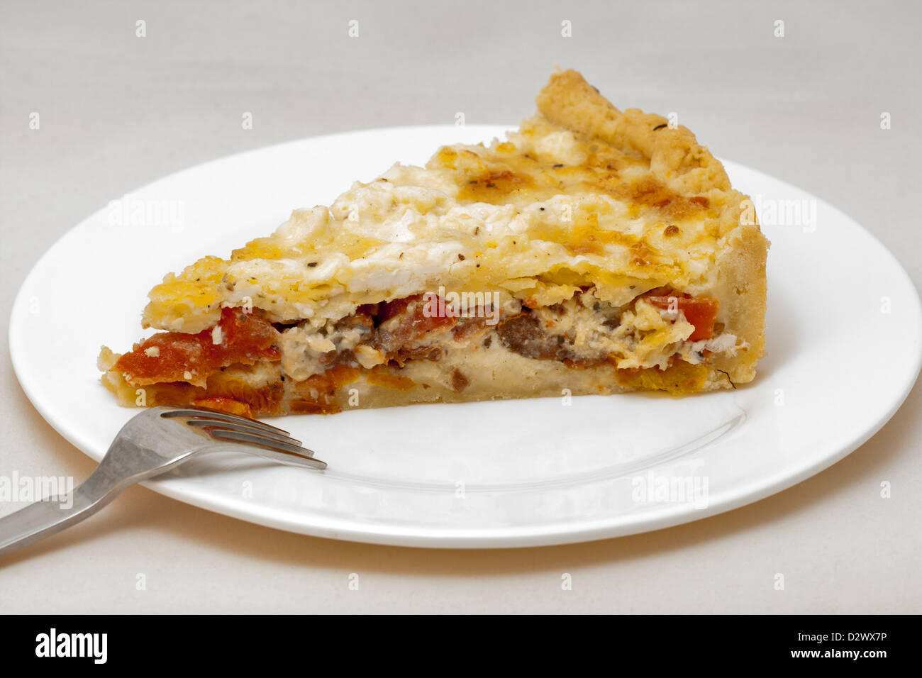 A piece of cheese pie with dried tomatoes on white plate Stock Photo